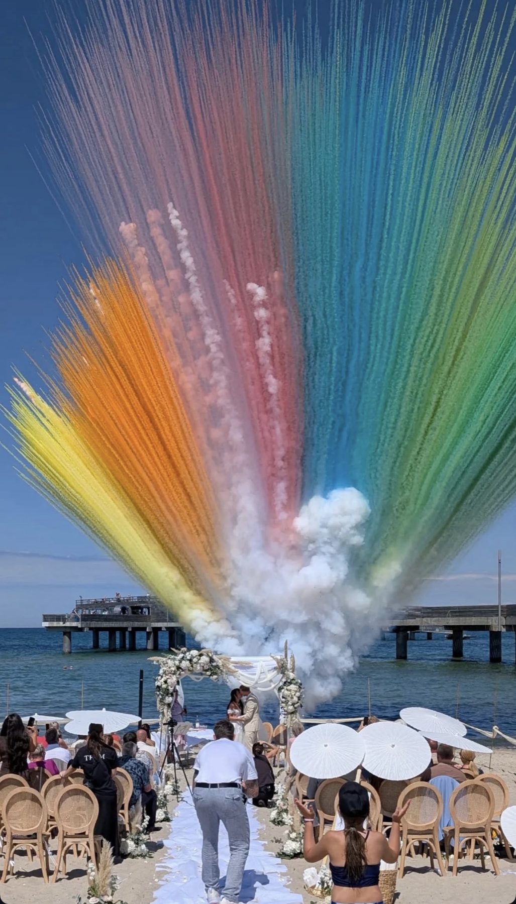 Regenbogenwand aus farbigem Rauch über einer Trauung an der Ostsee